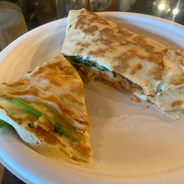 A savory crepe, cut in half, revealing a filling of meat, cheese, and green vegetables on a white plate.