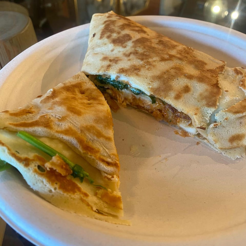 A savory crepe, cut in half, revealing a filling of meat, cheese, and green vegetables on a white plate.