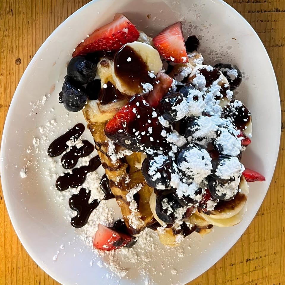 Creative Crêpes' waffle topped with strawberries, blueberries, bananas, chocolate syrup, and powdered sugar.