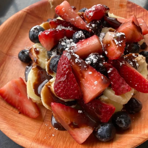 A Creative Crêpes dessert with strawberries, blueberries, bananas, chocolate drizzle, and powdered sugar.