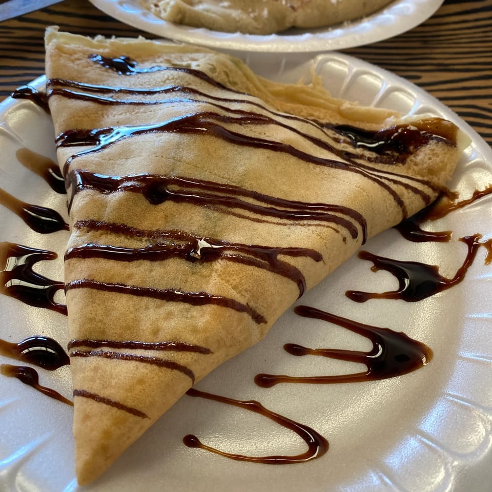 A Creative Crêpes chocolate drizzle crepe on a white plate, with more crepes in the background.