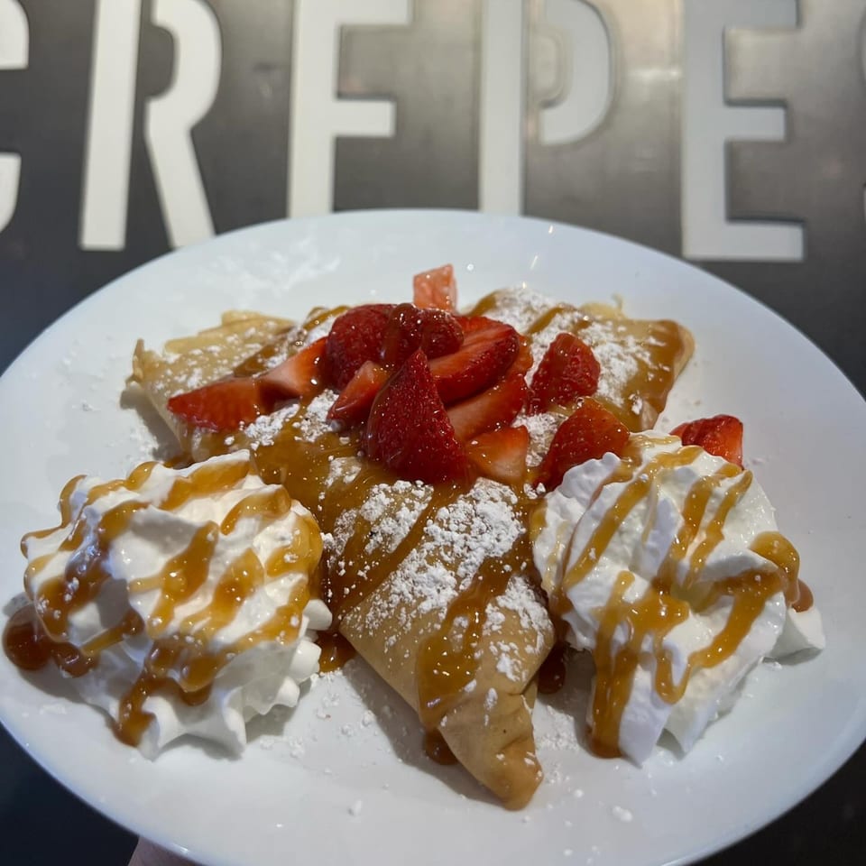Sweet crepes topped with fresh strawberries, whipped cream, caramel, and powdered sugar.