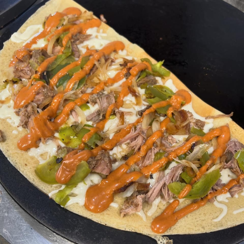 Savory Creative Crêpes crepe with shredded meat, green peppers, onions, cheese, and orange sauce.